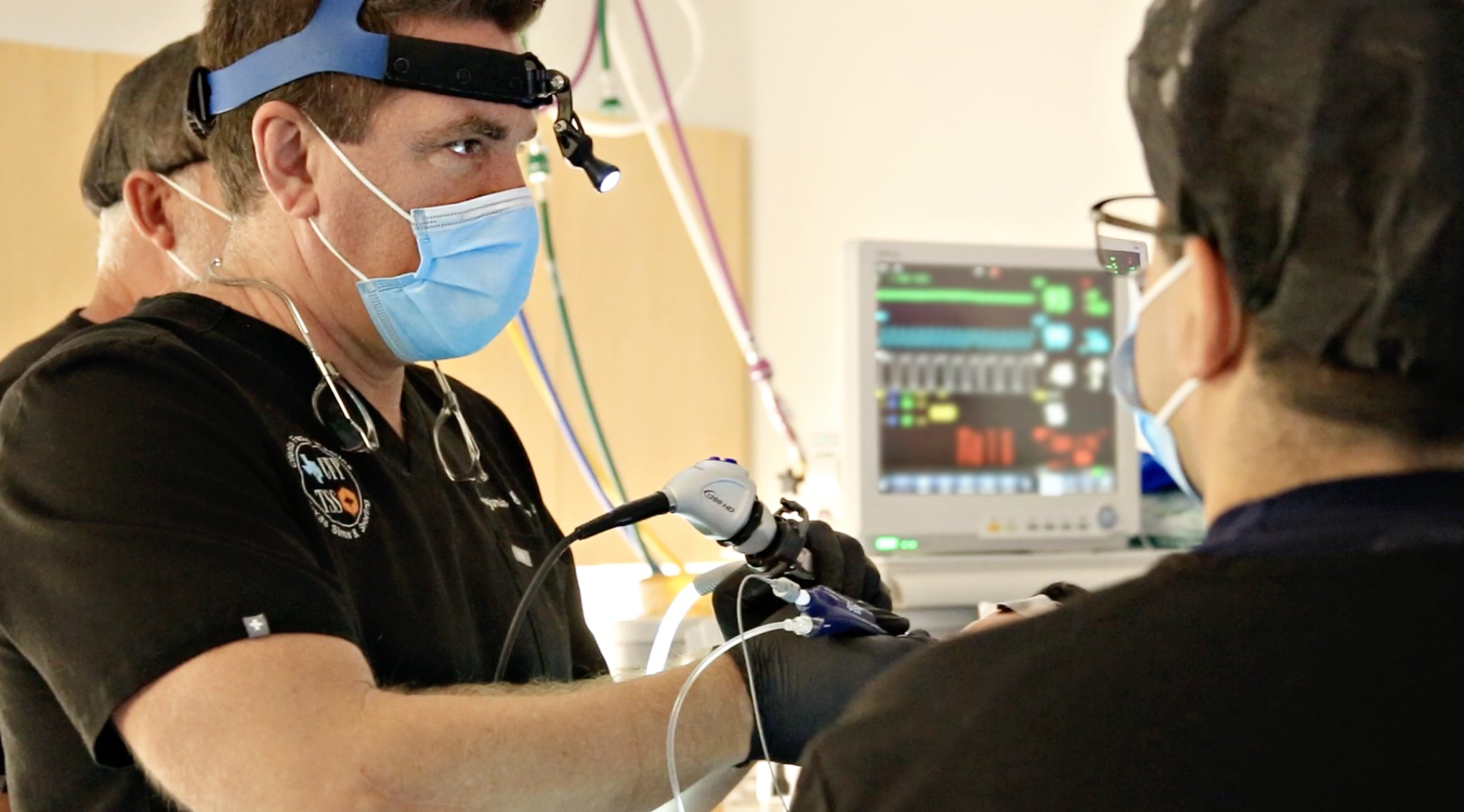 ENT surgeon performing endoscopic procedure on patient in clinical setting with monitoring equipment
